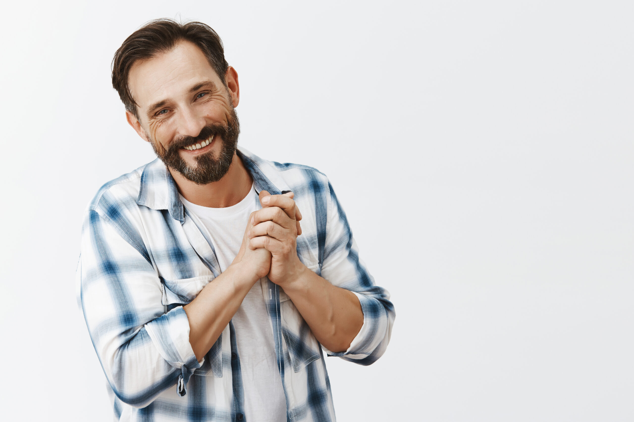 Father being pleased of cute and touching drawing of child, tilting head and smiling, holding palms together while standing over gray background in casual shirt and grinning from having great family